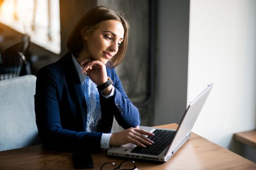 Smiling woman in eyeglasses using a laptop at home office with decor and November calendar.